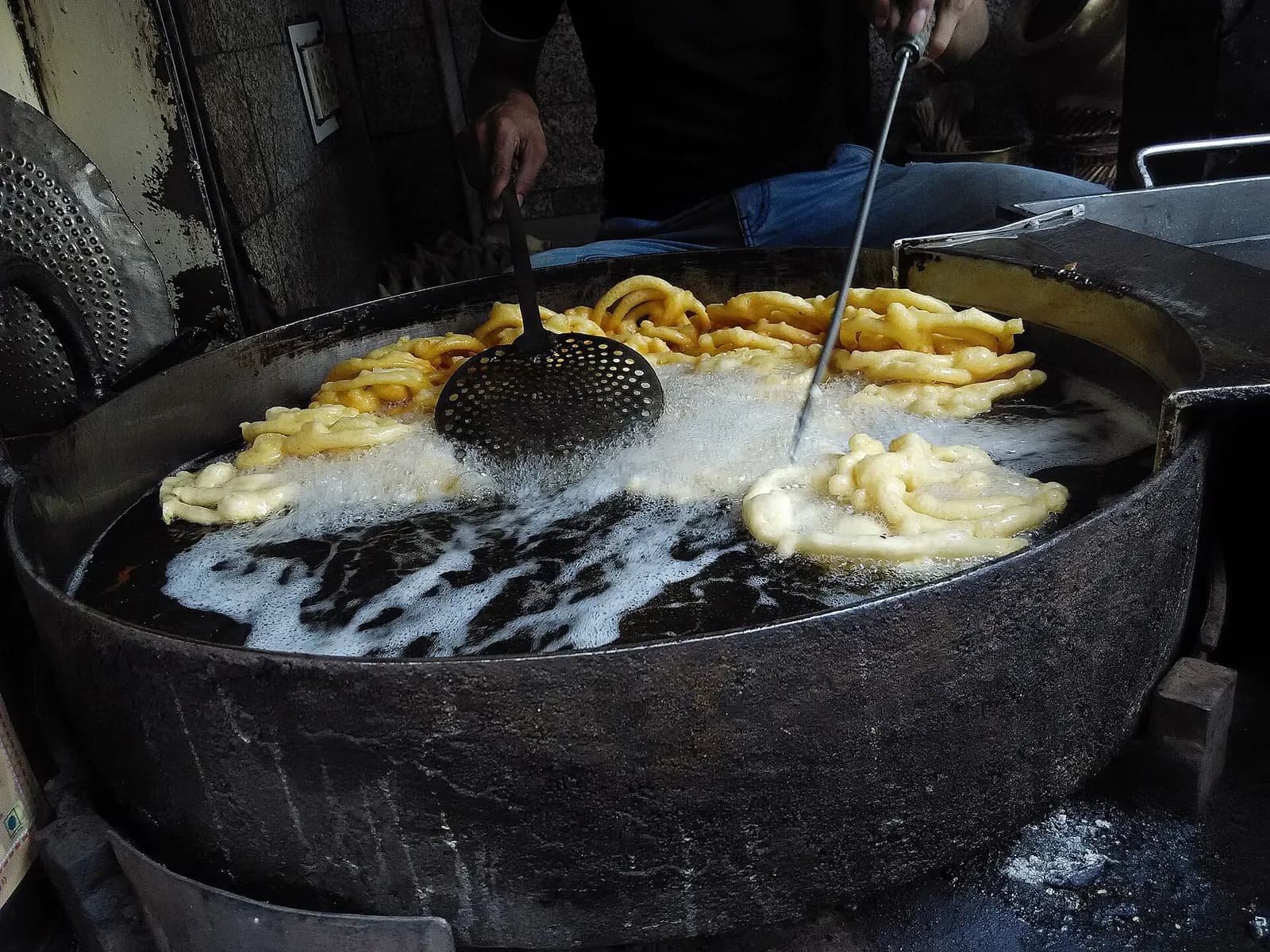 Jalebis frying in a large iron kadhai of oil at a sweet shop in Chandni Chowk, Delhi