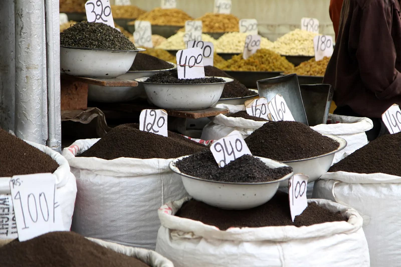 Sacks and bowls of loose tea leaves with handwritten price cards at a wholesale shop in Khari Baoli, Old Delhi