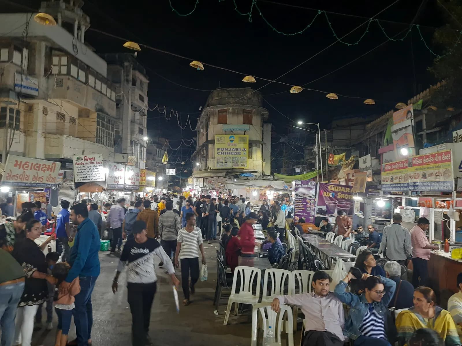 Crowds at the night food market in Manek Chowk, old Ahmedabad, with plastic chairs, food stalls and lit-up shop signs
