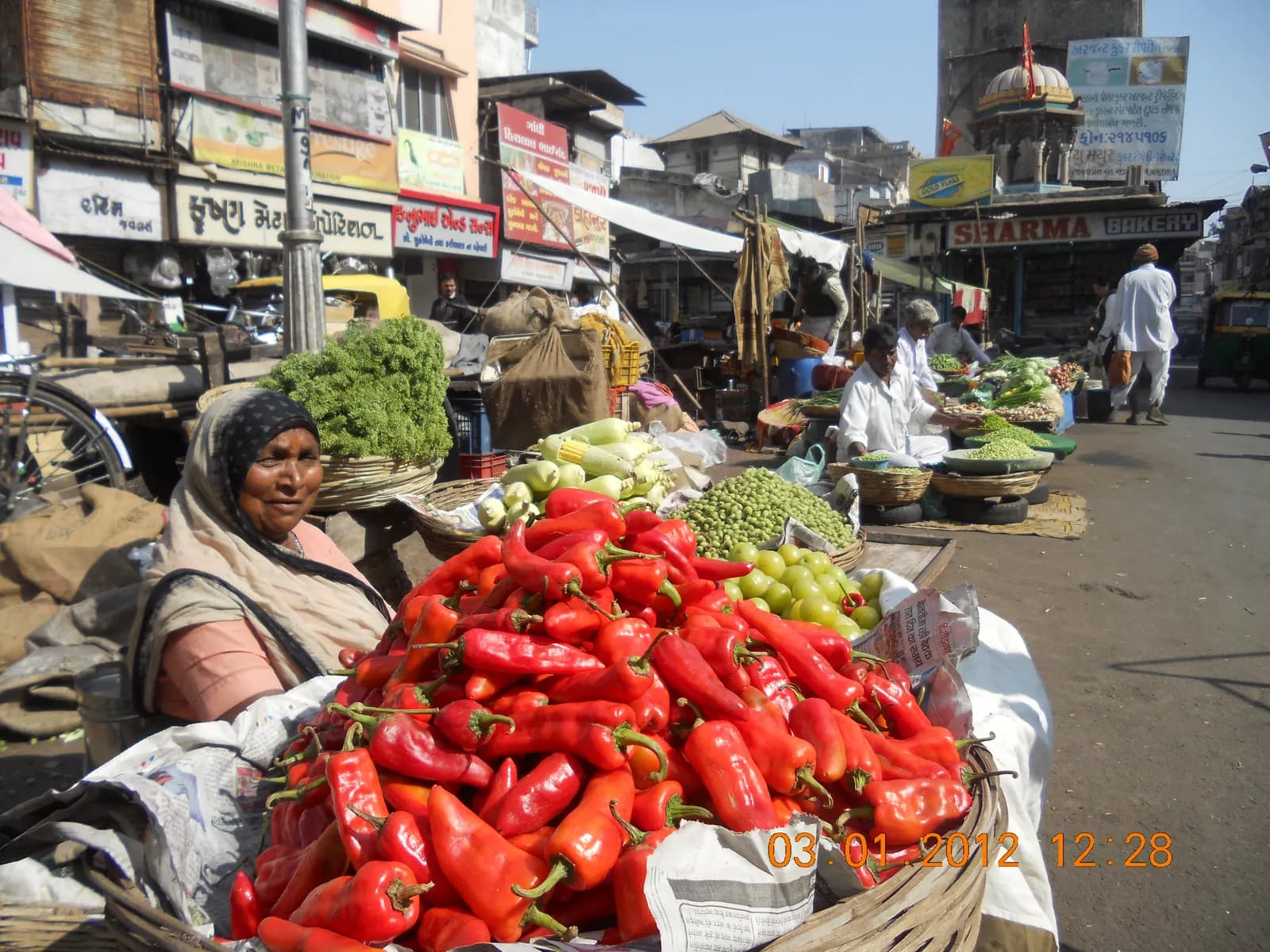 A vegetable seller with baskets of red chillies and capsicum at the Manek Chowk market in Ahmedabad, with shopfronts behind