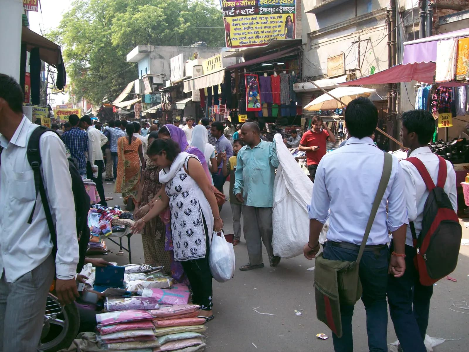 Shoppers and pavement sellers on a crowded market street in old Gurgaon lined with clothing shops