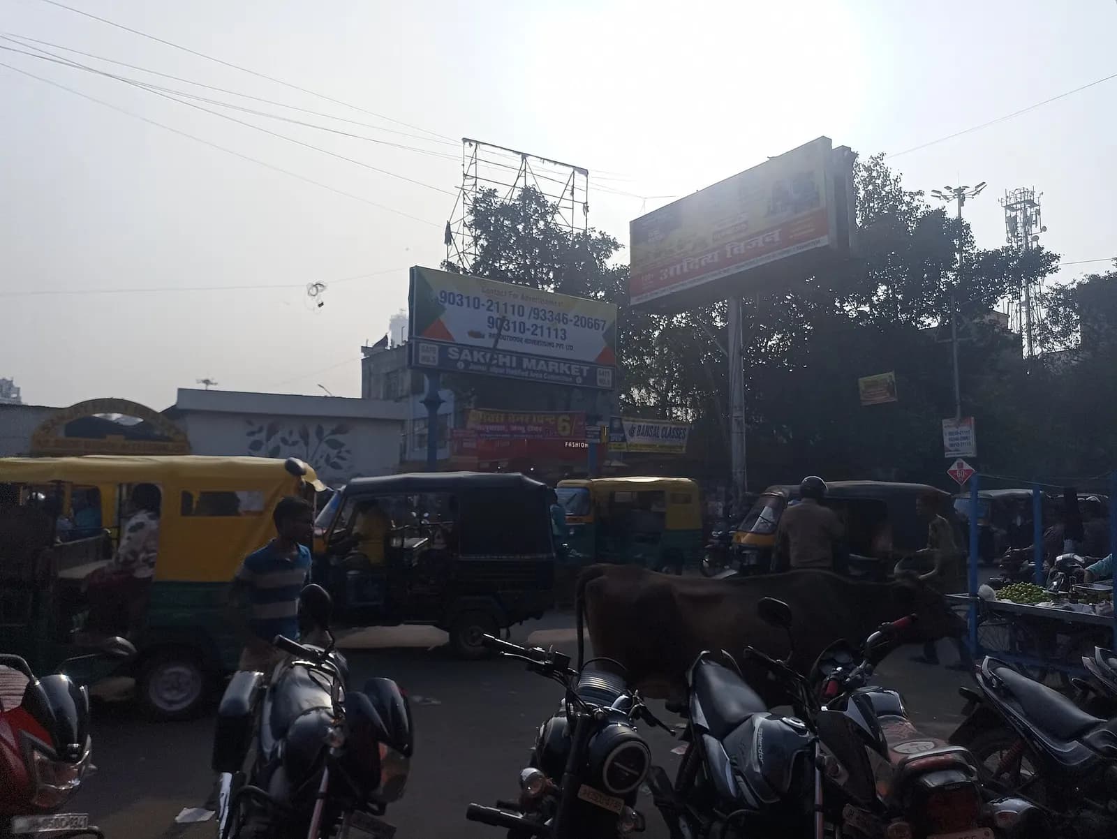 Auto-rickshaws and parked motorcycles at the edge of a busy market in Jamshedpur