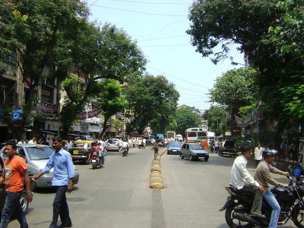 Lamington Road in south Mumbai, lined with trees and ground-floor shops, with traffic and pedestrians