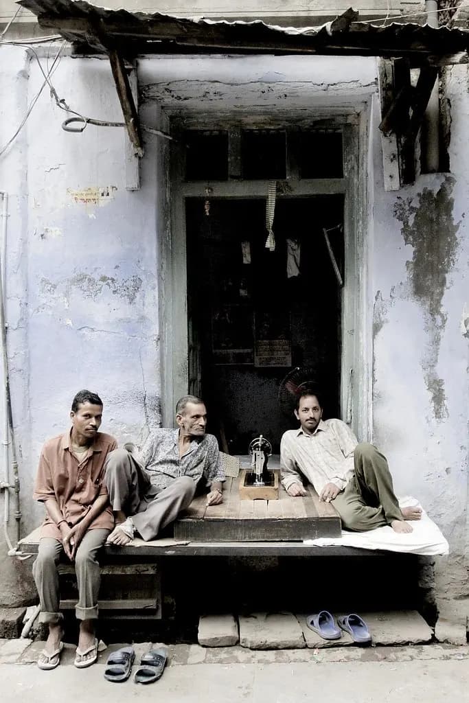 Three tailors sitting outside a small tailoring shop with a sewing machine in an old Amritsar street