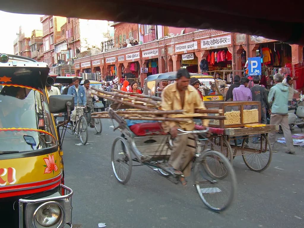 Cycle-rickshaws and auto-rickshaws passing a row of shops with Hindi signboards in Jaipur's walled Pink City
