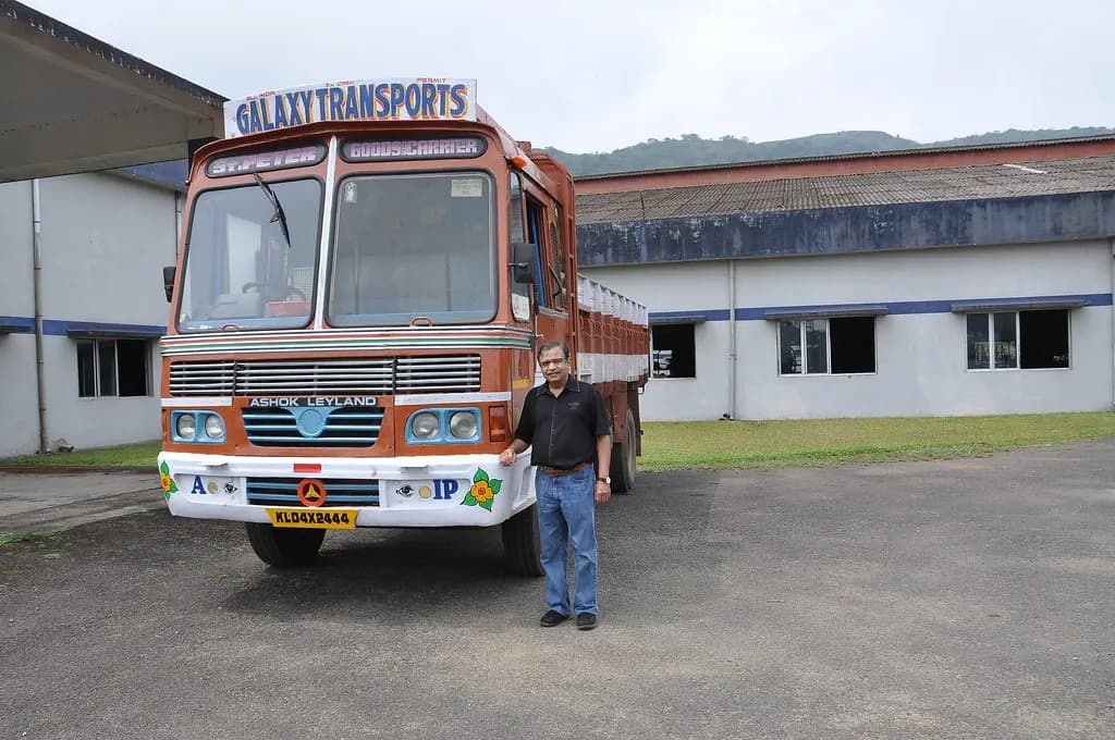 A man standing beside a painted Ashok Leyland goods lorry parked outside a warehouse in India