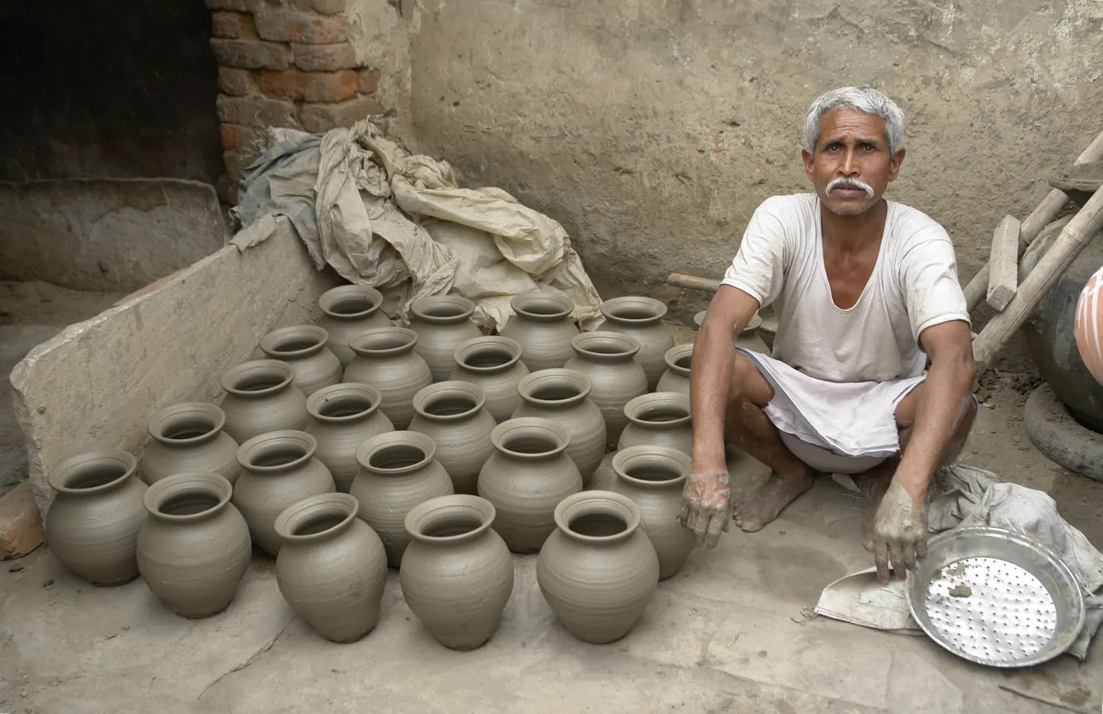 A potter in Jaura, India, sitting beside rows of freshly made clay pots