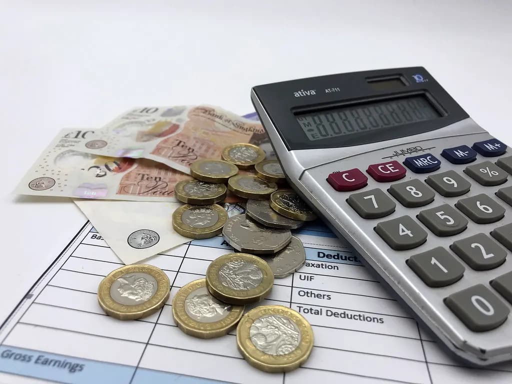Pound coins and ten-pound notes on a printed payslip showing gross earnings and deductions, next to a calculator