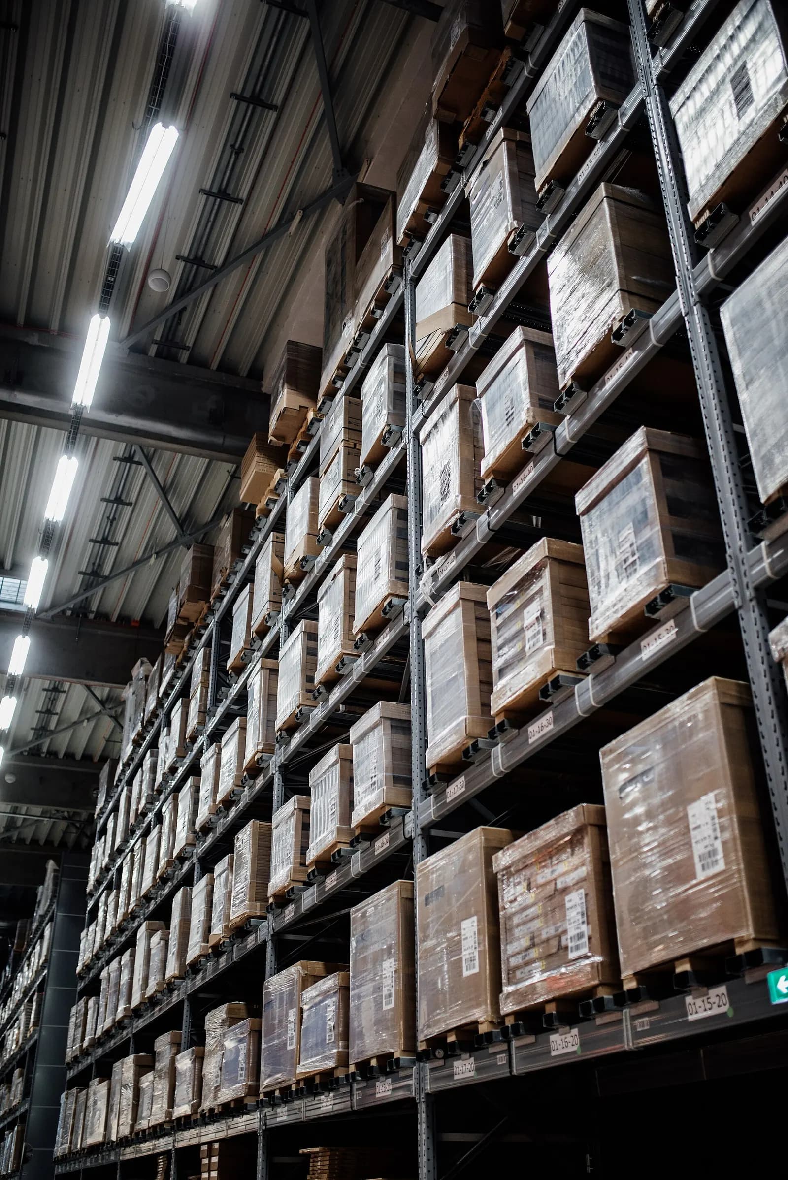 High warehouse racking stacked with shrink-wrapped pallets under strip lighting