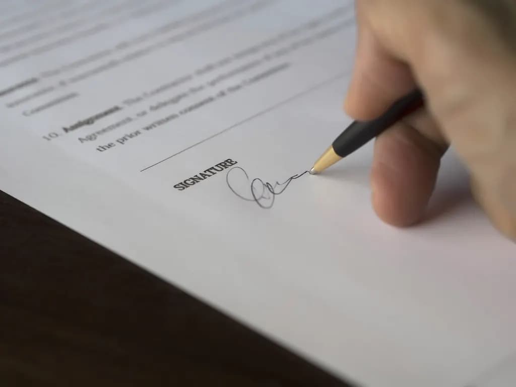 Close-up of a hand signing the signature line of a printed contract with a ballpoint pen