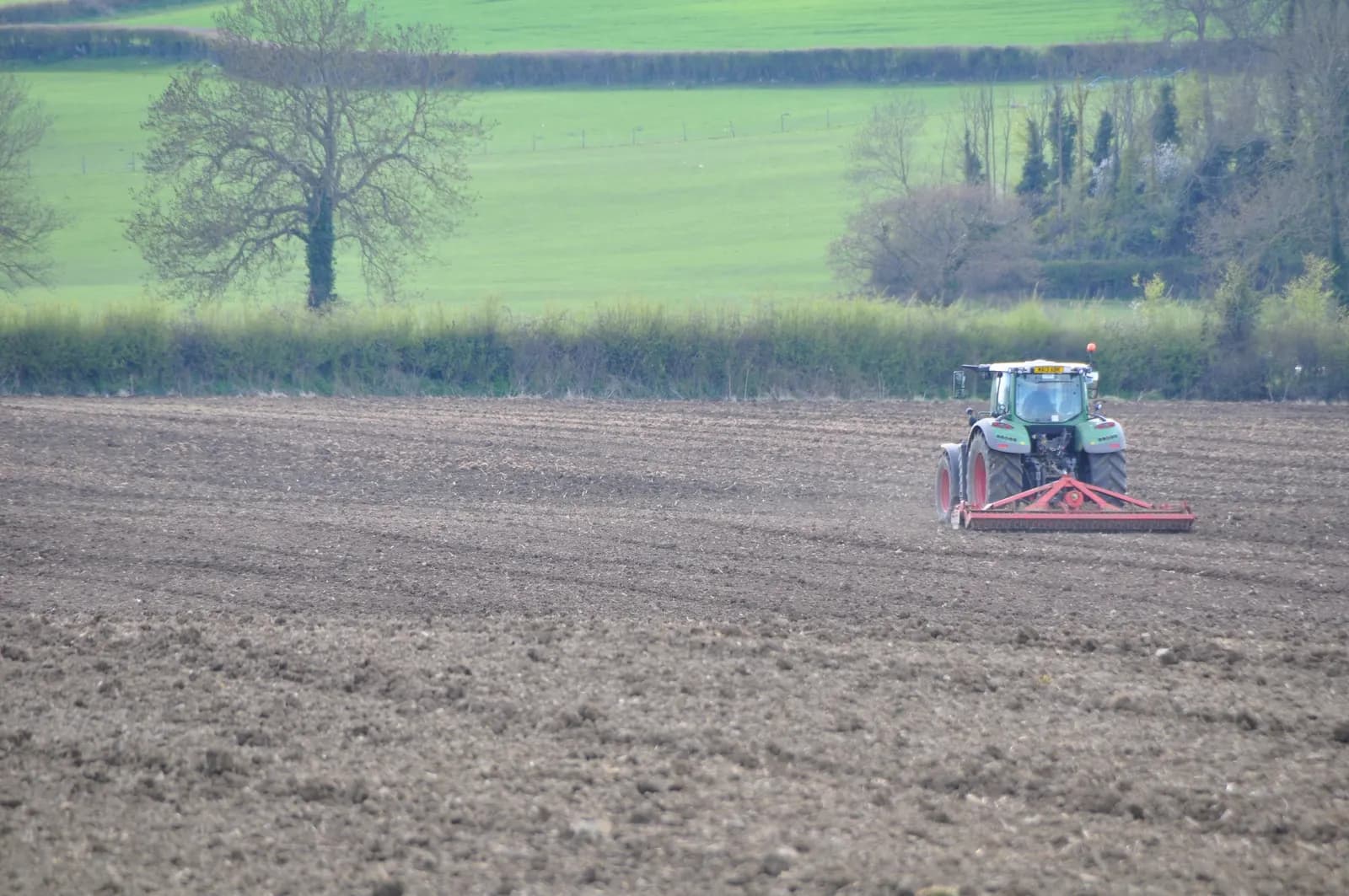 A tractor working a freshly ploughed field in West Somerset with hedgerows and hills behind