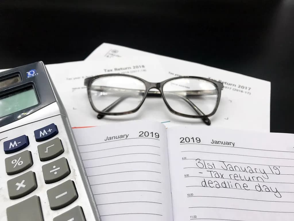 Self Assessment tax return forms beside a calculator, glasses and a diary page marked 31 January tax return deadline day