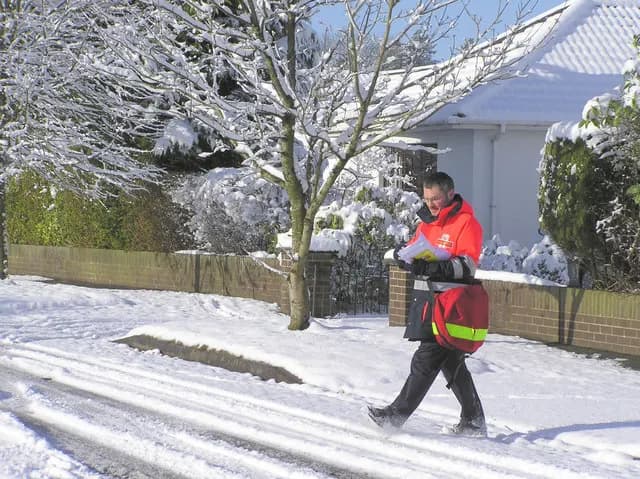 A Royal Mail postman delivering letters along a snowy residential street