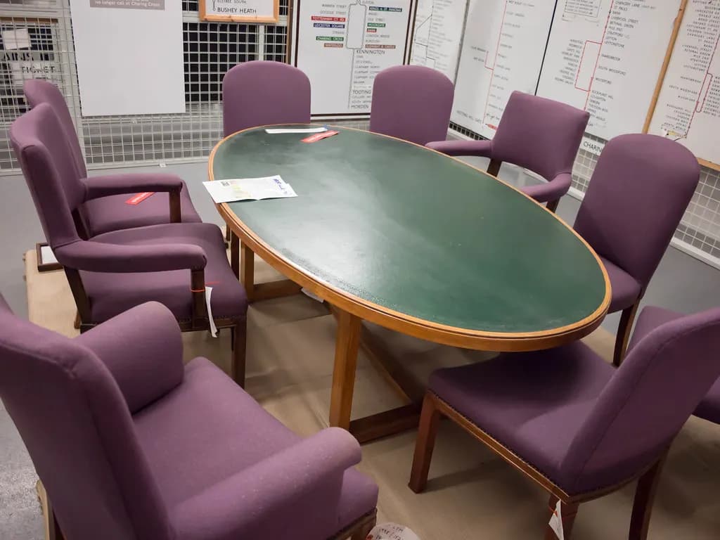 An oval boardroom table with a green leather top surrounded by purple upholstered chairs