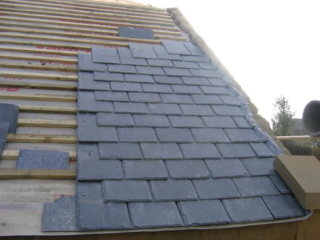 A pitched roof part-way through re-slating, with new grey slates fixed over battens and breathable membrane