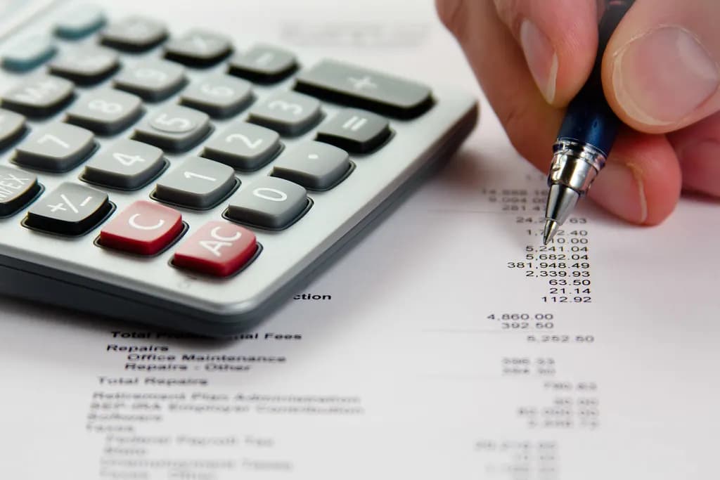 Calculator beside a printed list of business costs being checked with a pen