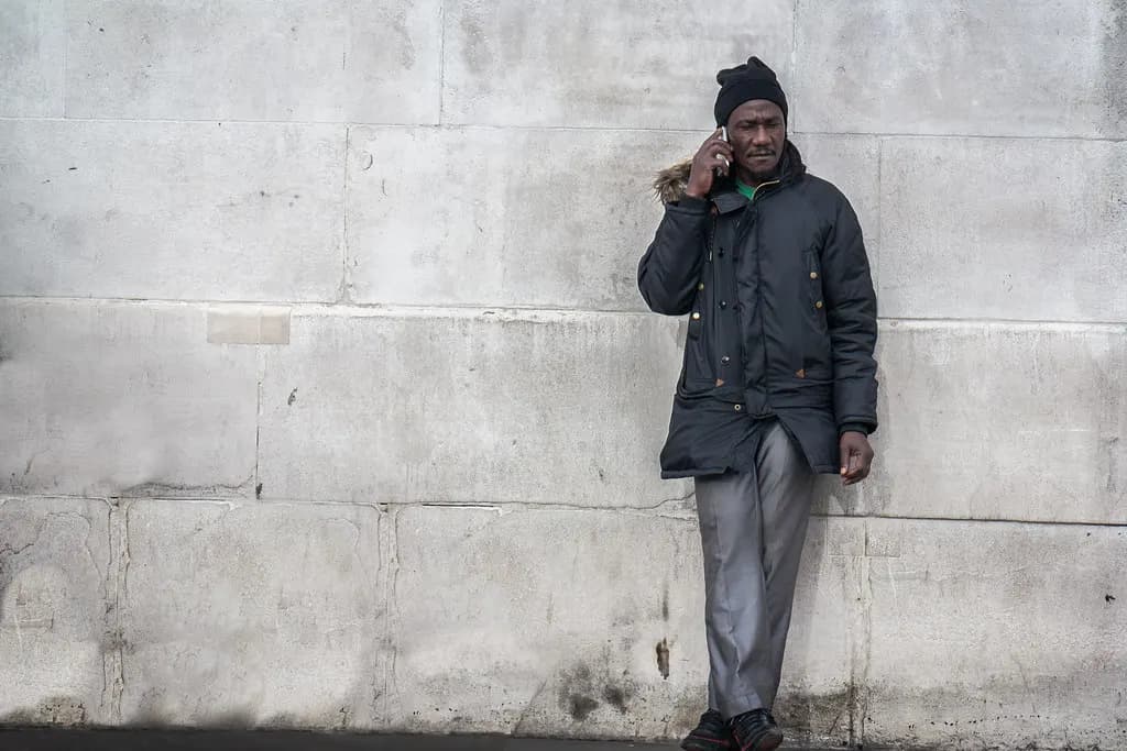 Man in a winter coat making a mobile phone call while leaning against a stone wall