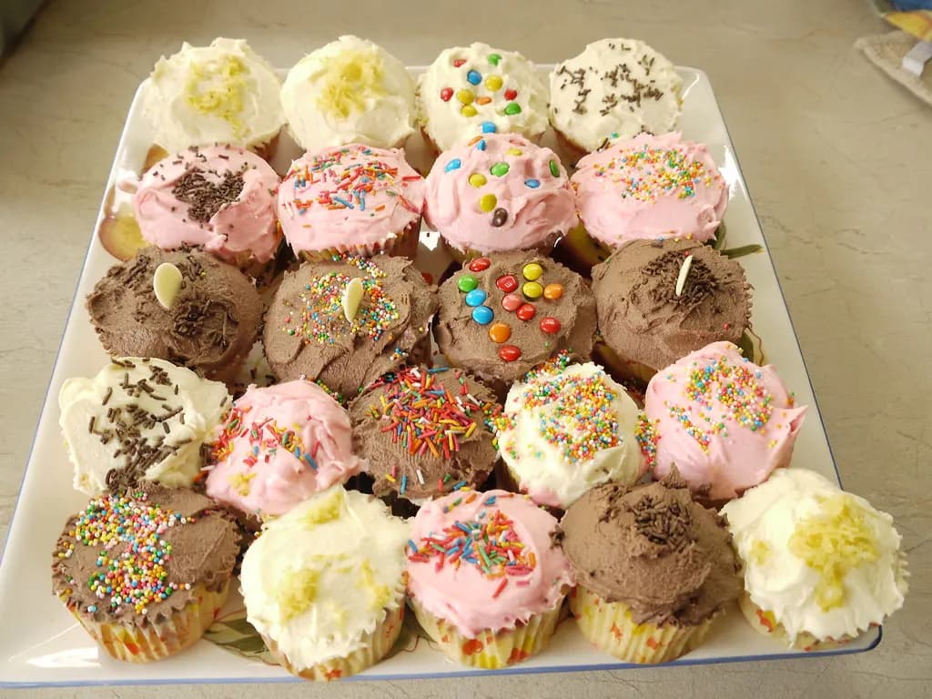 A plate of homemade cupcakes with pink, white and chocolate icing and sprinkles
