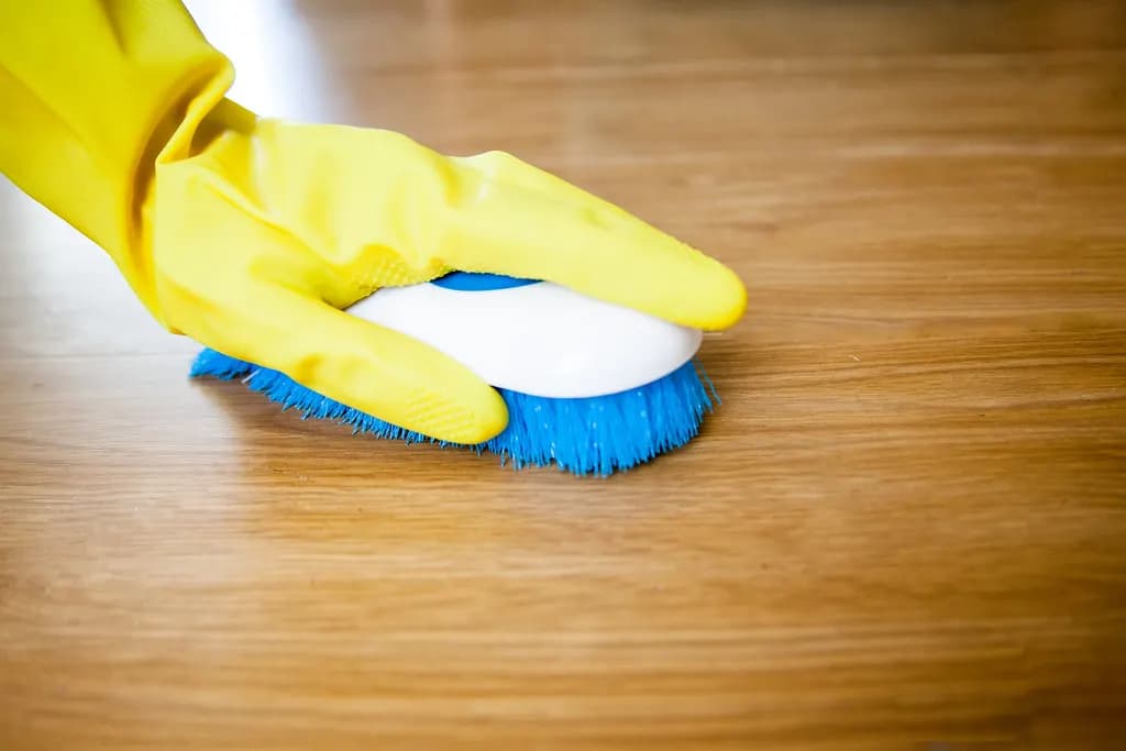 Hands in yellow rubber gloves scrubbing a wooden table with a brush