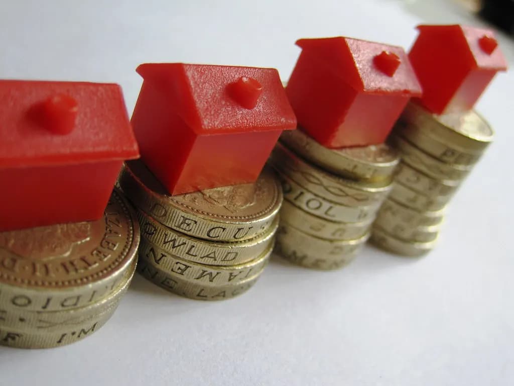 Red model houses standing on stacks of pound coins