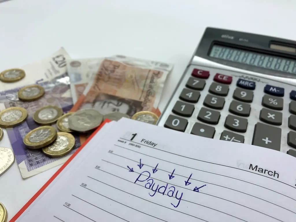 A diary page with payday written on the first of the month next to pound coins, banknotes and a calculator
