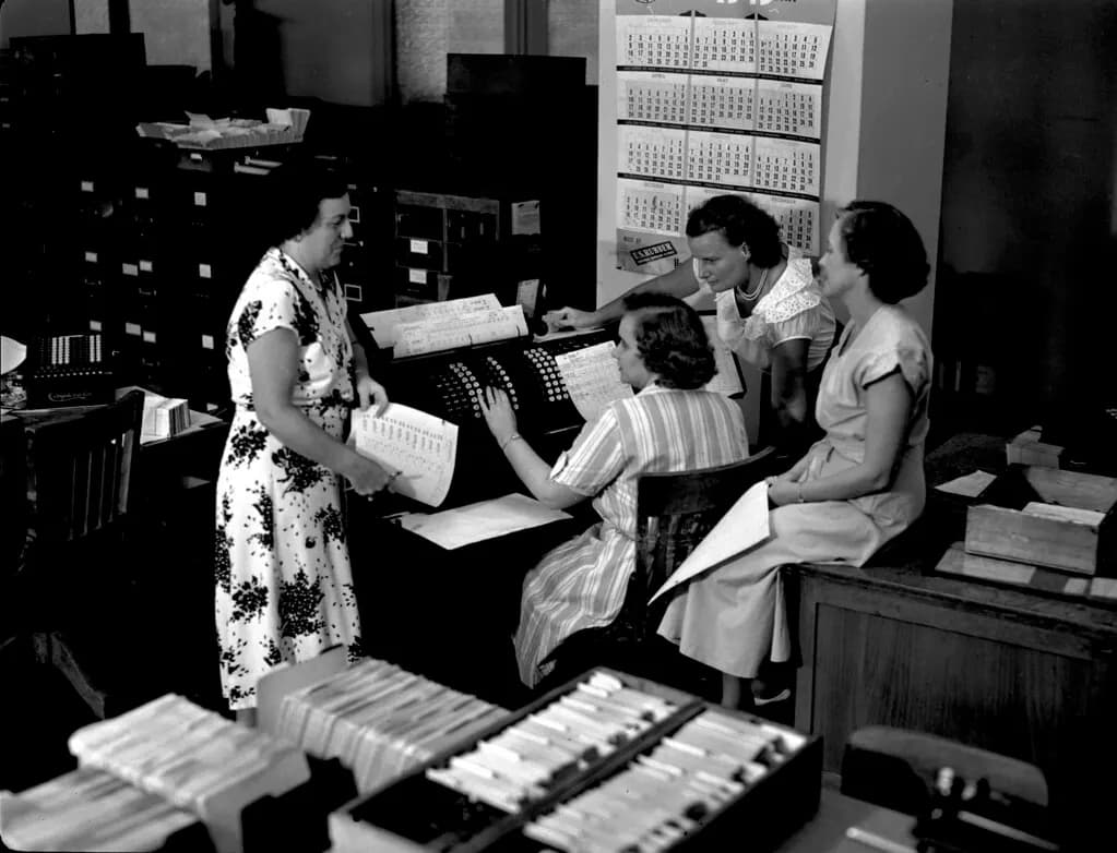 Black and white photo of clerks working at a payroll machine in a 1950s company payroll department