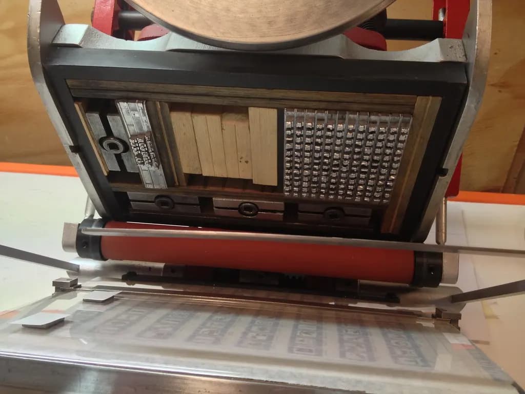 A small letterpress printing press loaded with type and an ink roller, ready to print a sheet of labels