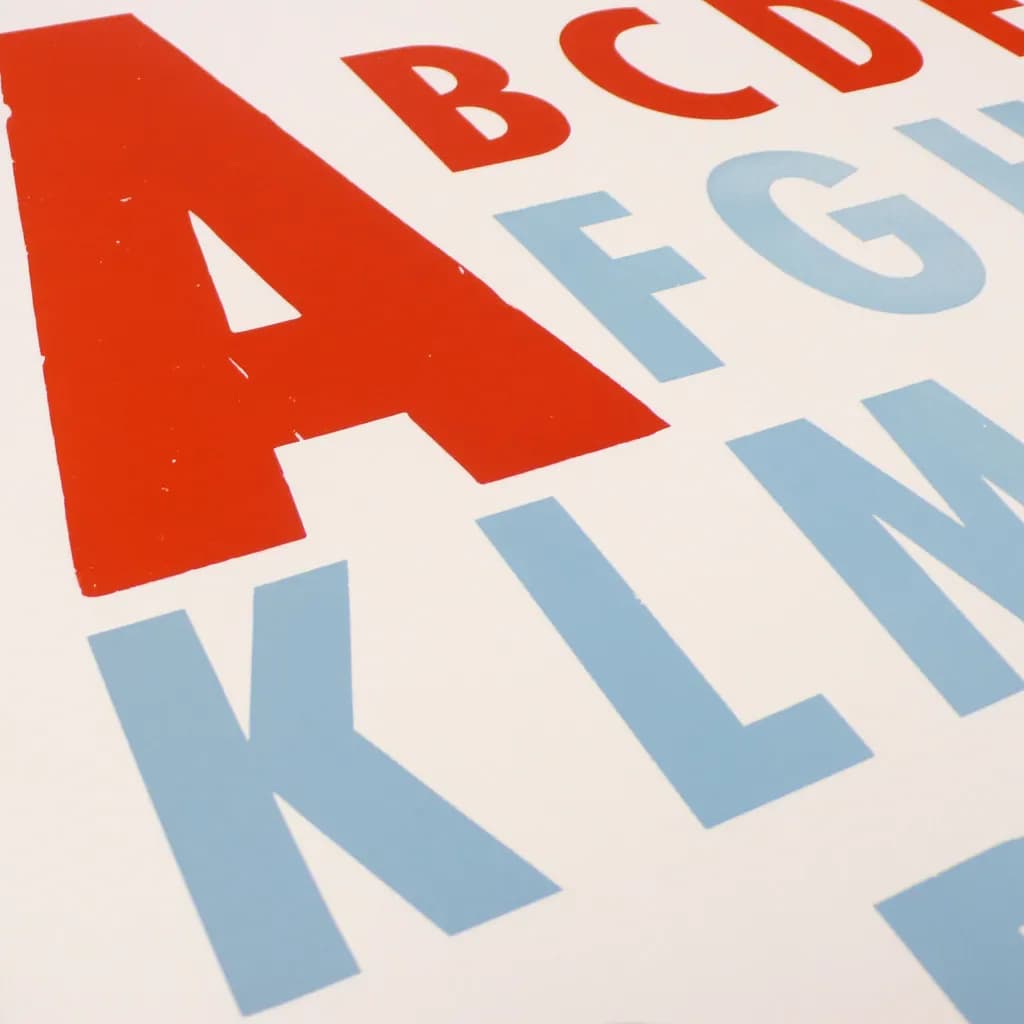 Large red and pale blue capital letters printed from wooden type on white paper