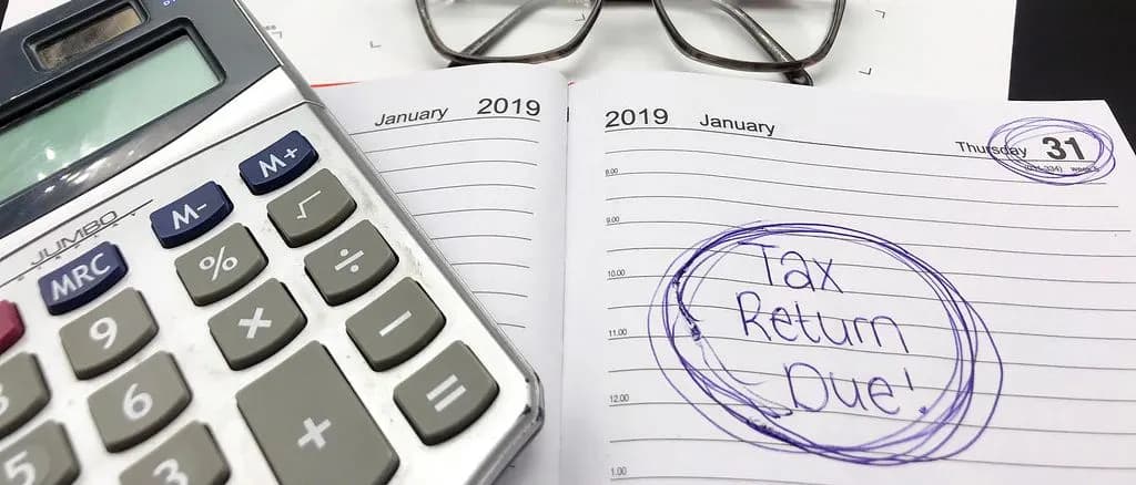 A diary open at 31 January with 'Tax Return Due!' circled, next to a calculator and reading glasses