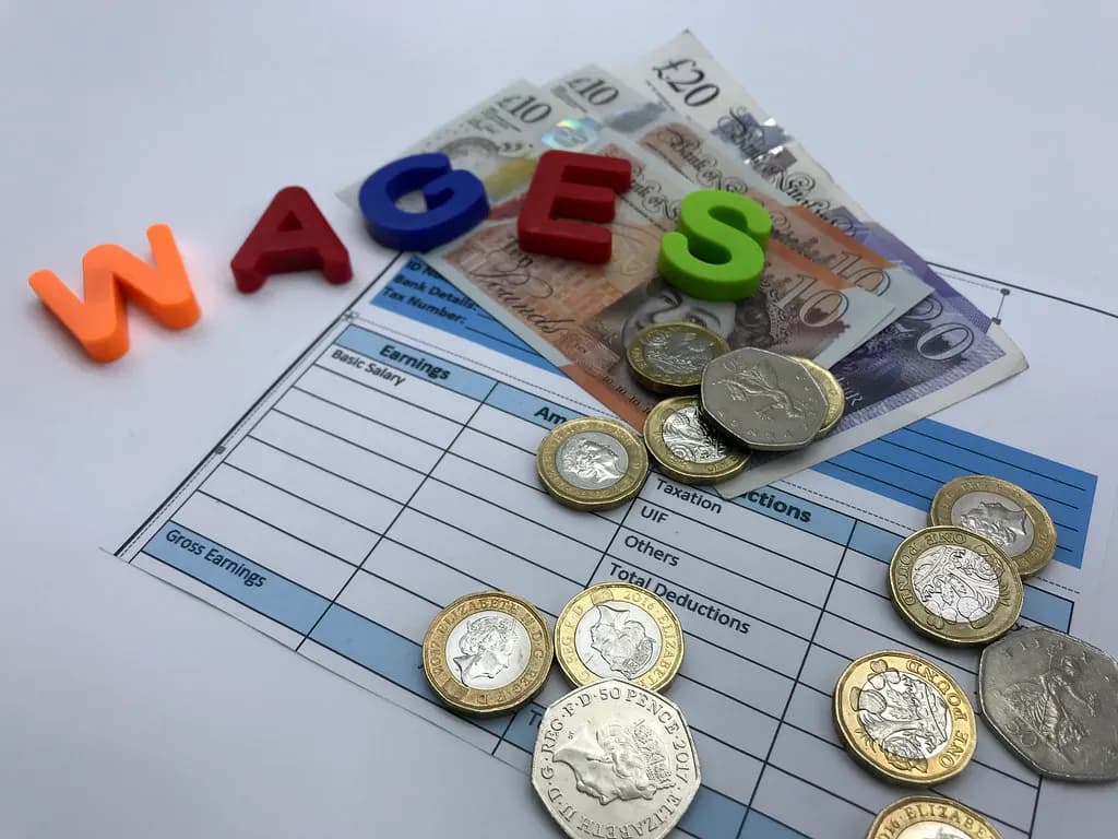 The word wages spelled out in coloured letter tiles beside British coins and banknotes