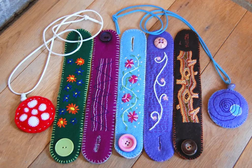 Handmade felt bracelets and pendants with embroidery and buttons laid out on a wooden table