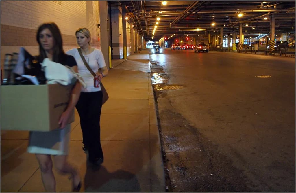 A woman walking along a street carrying a cardboard box of belongings from her office