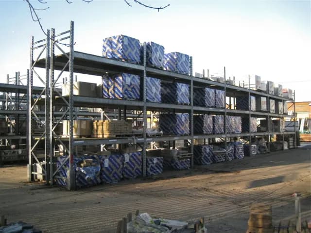 Wrapped packs of paving slabs stacked on tall steel racking in a builders' merchant yard