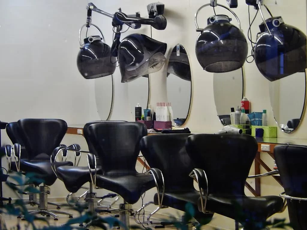 Black styling chairs in front of mirrors with hood dryers mounted above them