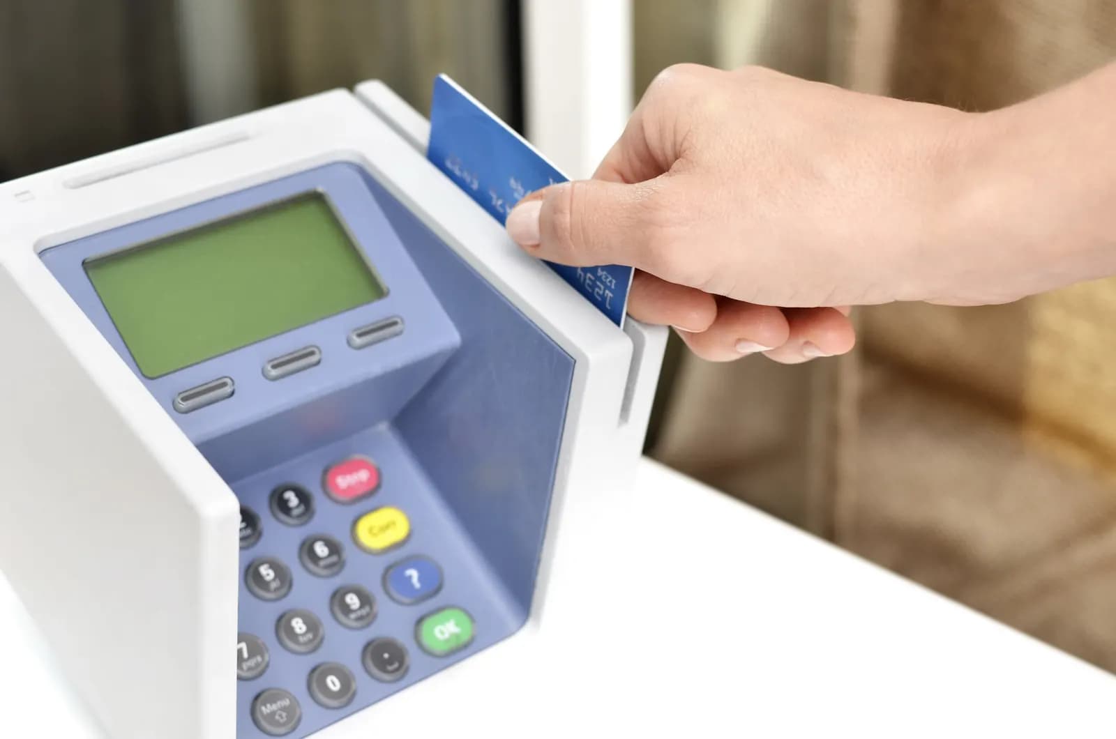 A hand inserting a credit card into a countertop card payment terminal