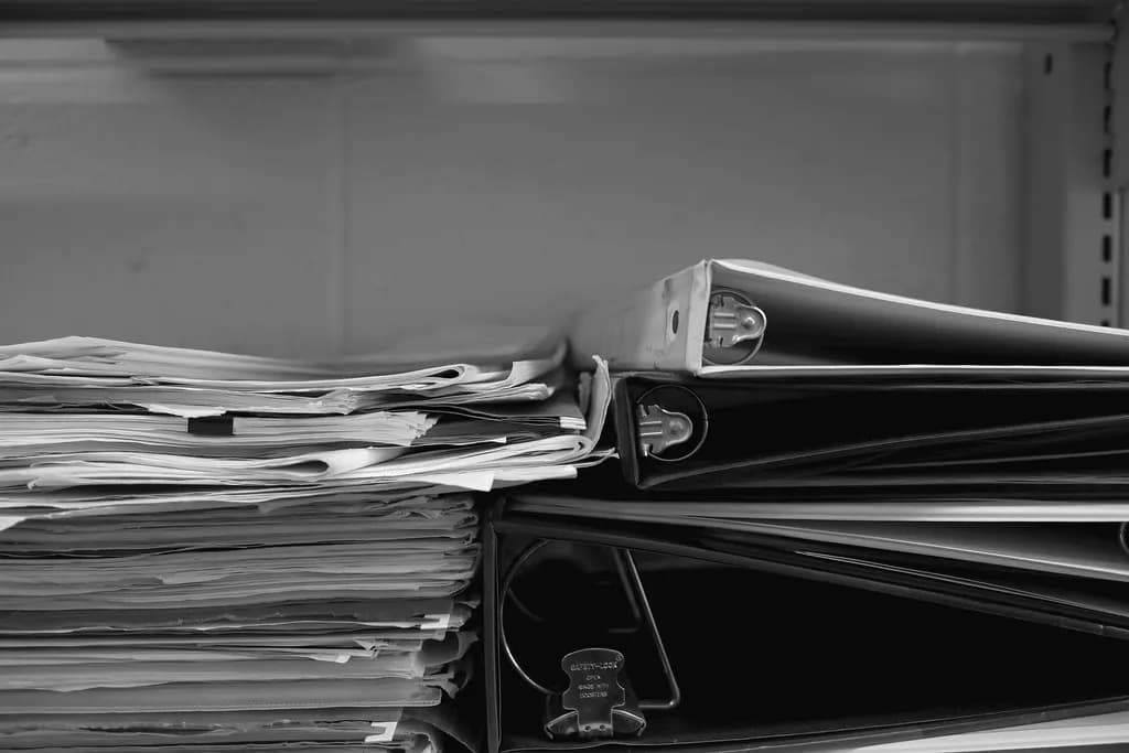 Black-and-white photo of binders and loose papers stacked on an office shelf