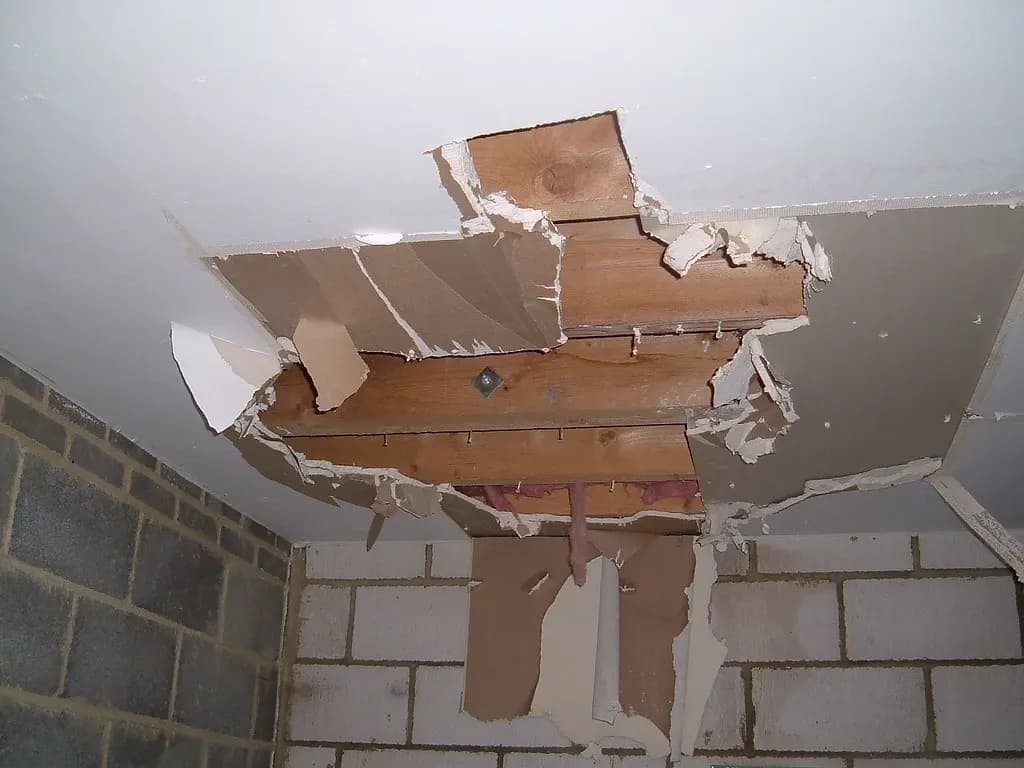 Ceiling plasterboard torn open after water damage, exposing joists above a block wall