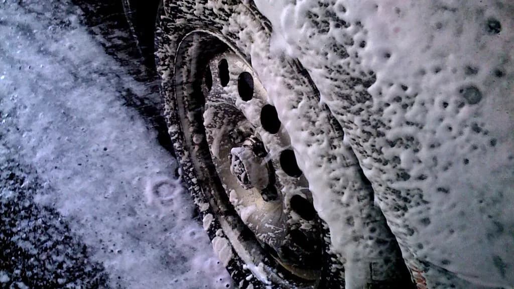 Thick wash foam covering a car wheel and tire on a wet wash bay floor
