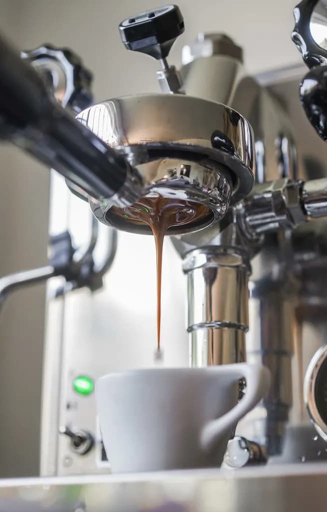 Espresso pouring from a bottomless portafilter into a white cup on a stainless espresso machine