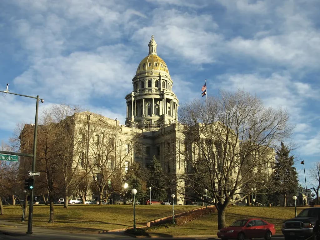 The Colorado State Capitol in Denver with its gold dome, seen across a lawn with bare winter trees