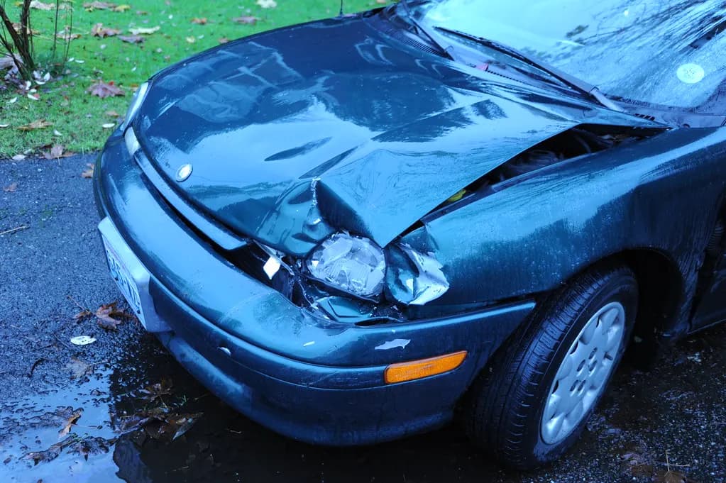 Green sedan with a crumpled hood and broken headlight after a front-end collision