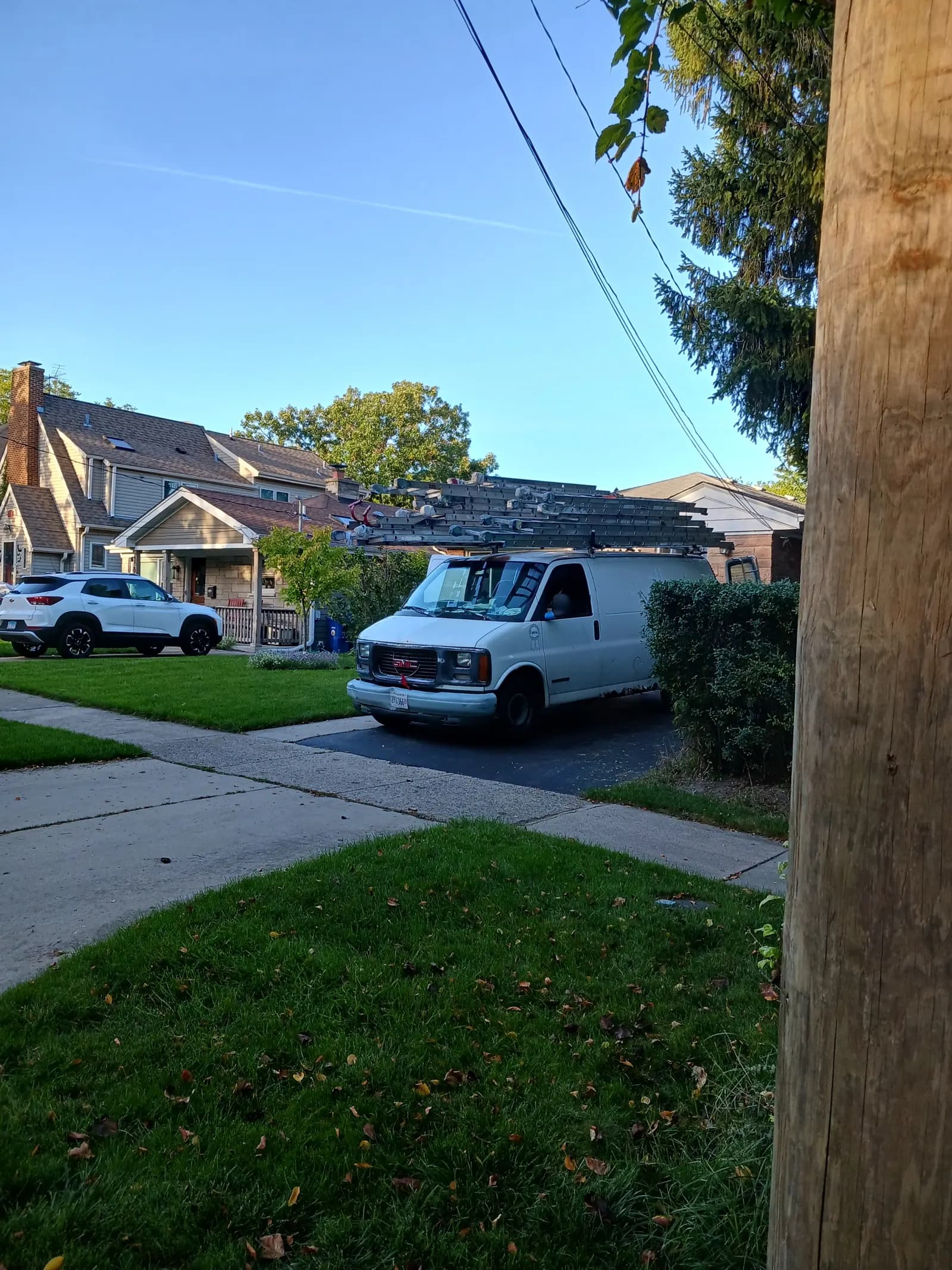White work van with a roof rack loaded with ladders parked in a residential driveway