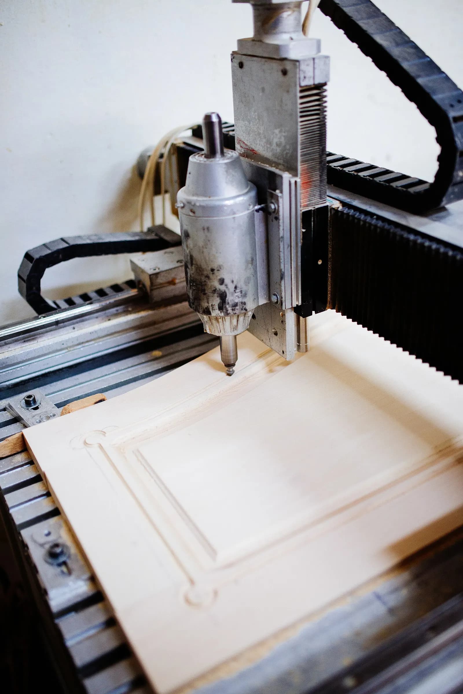 CNC router carving a raised-panel pattern into a wooden board in a workshop