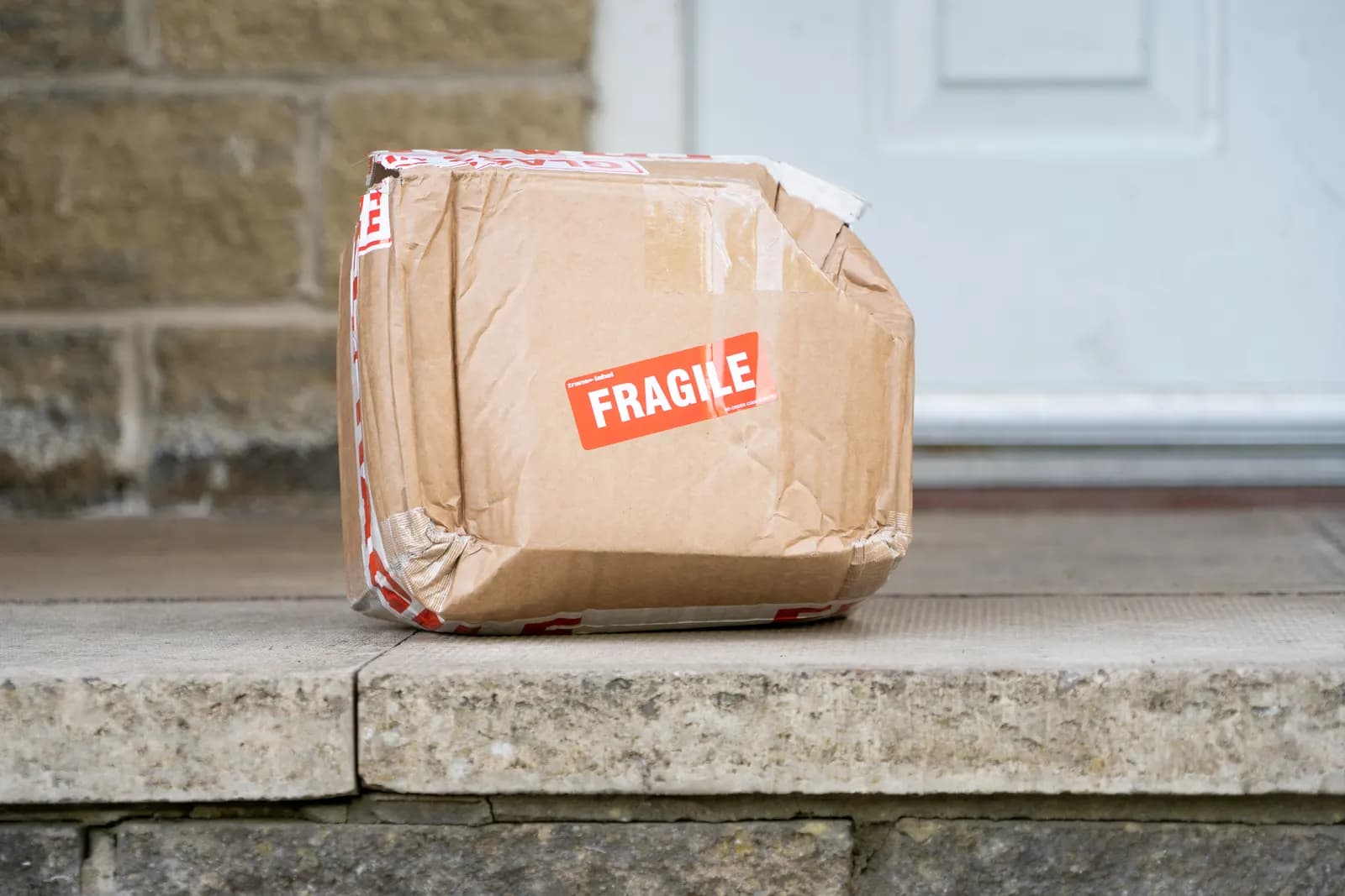A taped cardboard parcel marked Fragile left on a stone doorstep