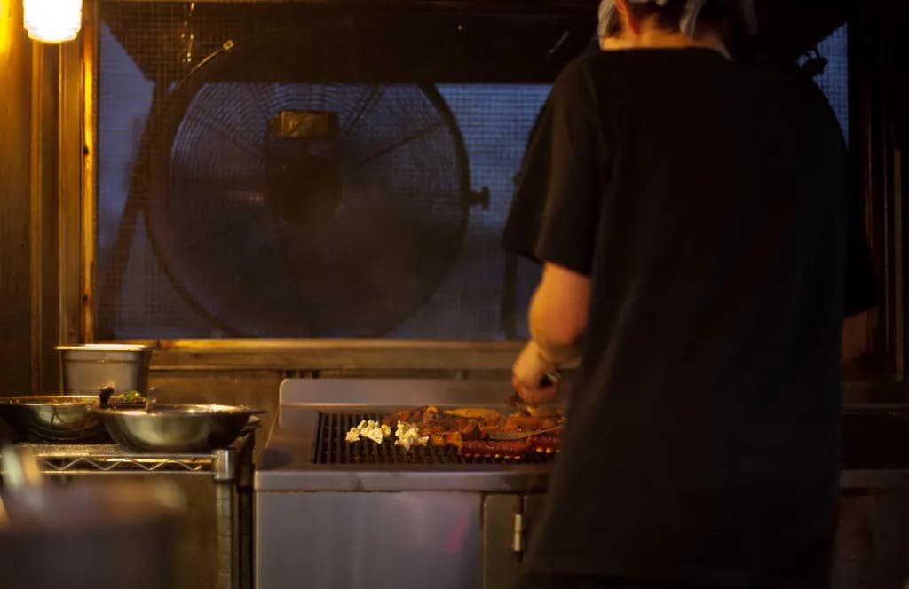 A cook working at a grill under an exhaust hood inside a food trailer at night