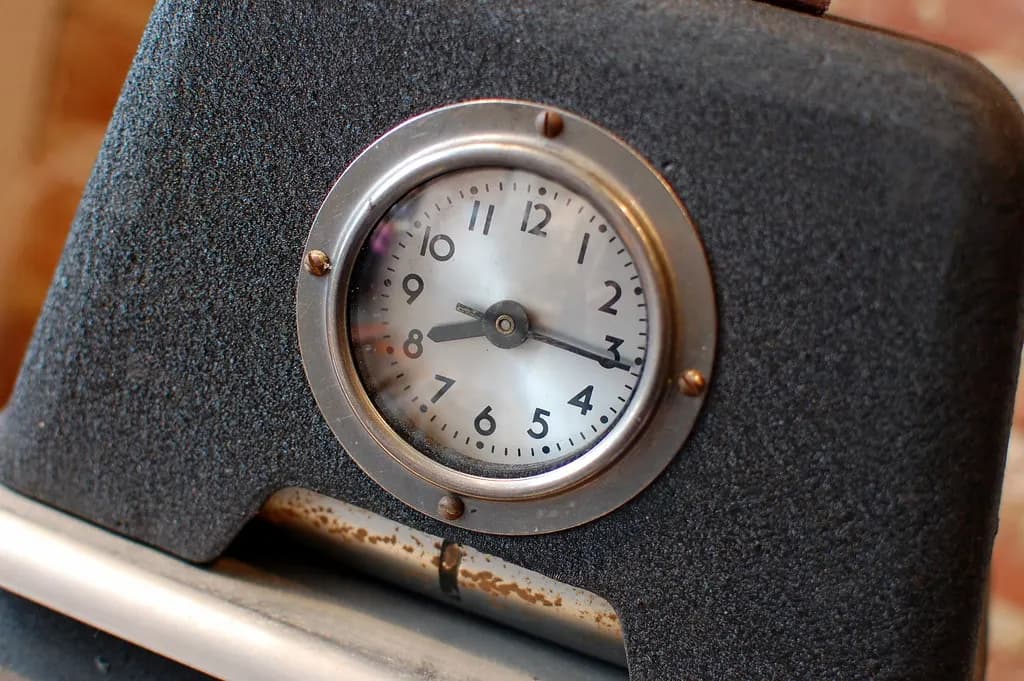 A mechanical punch clock on a wall with a rack of paper time cards beside it