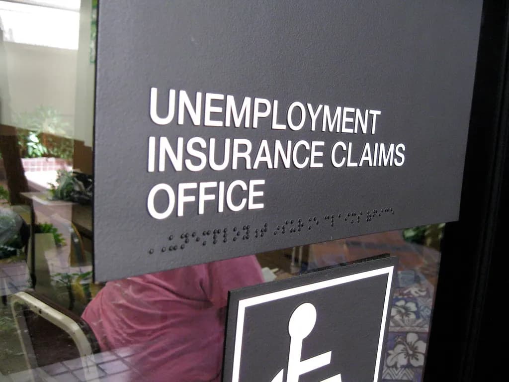 Sign reading Unemployment Insurance Claims Office with braille lettering beside a glass door
