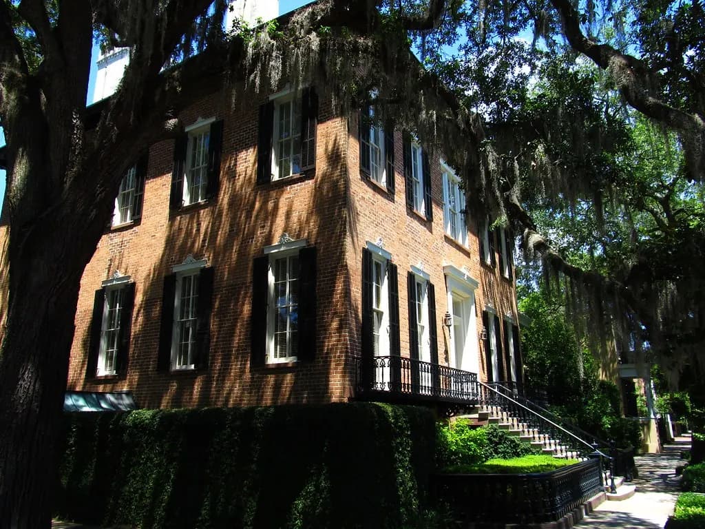 Brick townhouse with black shutters under live oaks at Abercorn and Jones Streets in Savannah