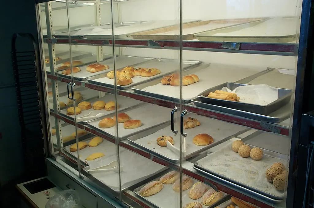 Glass bakery display case with trays of buns and pastries on several shelves