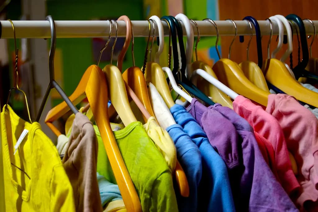 Rack of brightly colored shirts on yellow and wooden hangers in a clothing shop